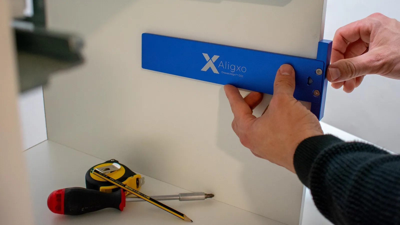 A carpenter holds the blue DrawerAlign D32 square against a cabinet side panel