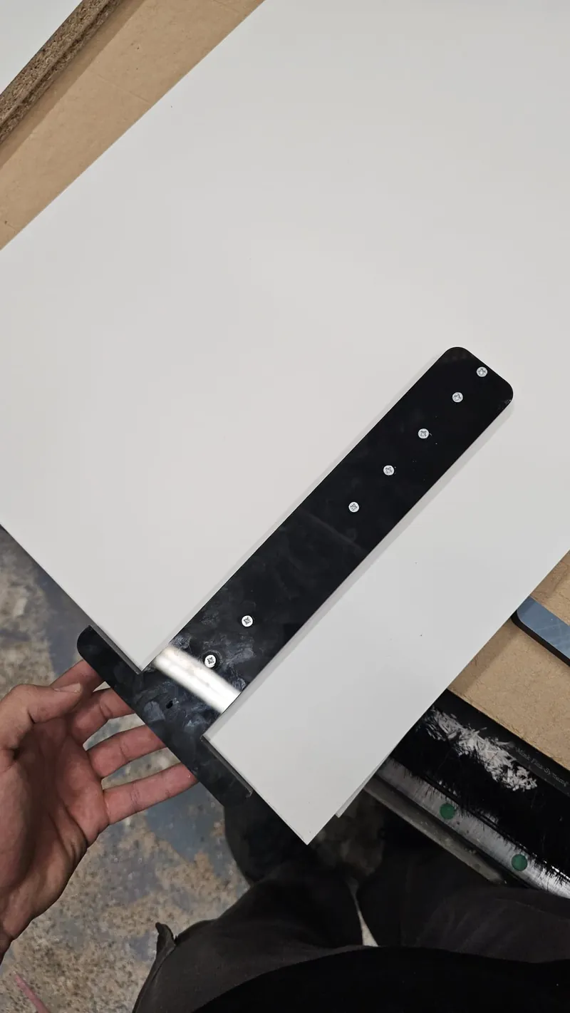Early black CNC-machined prototype of the drawer slide jig against a cabinet panel
